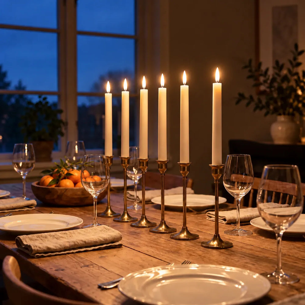 Zes brandende Wove Luma LED-dinerkaarsen in messing kandelaars op een gedekte eettafel op een winteravond