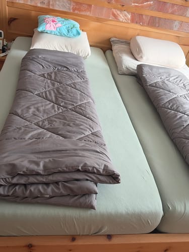 Twee matrassen naast elkaar met een grijs Wove-dekbed in een huisje met houten plafond