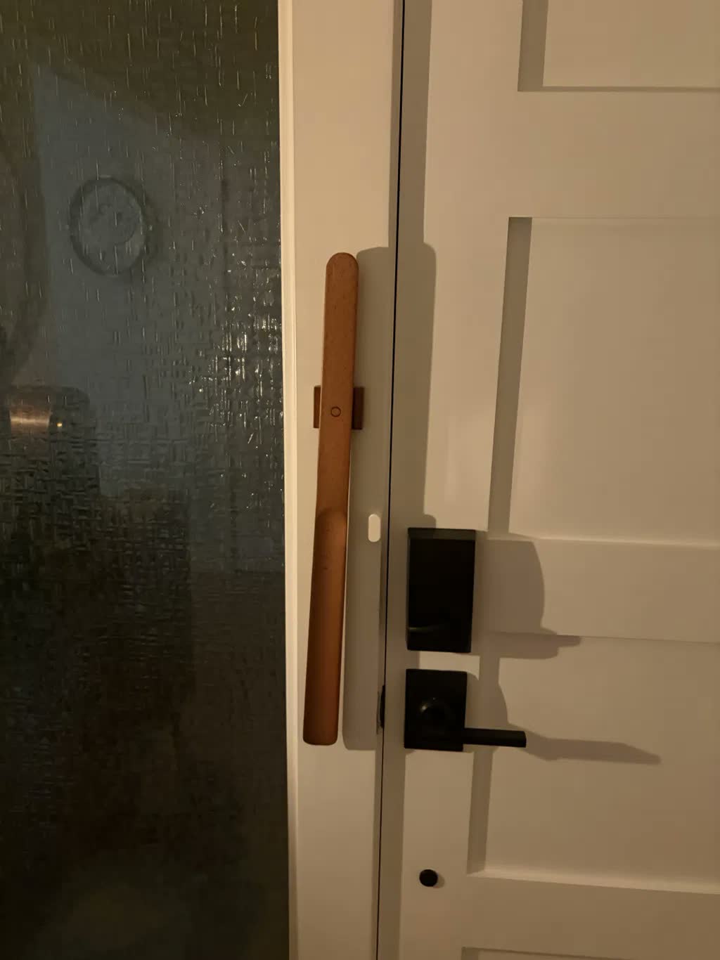 Schoenlepel van licht beuken magnetisch bevestigd op een witte deurpost naast een zwarte klink en een slim slot