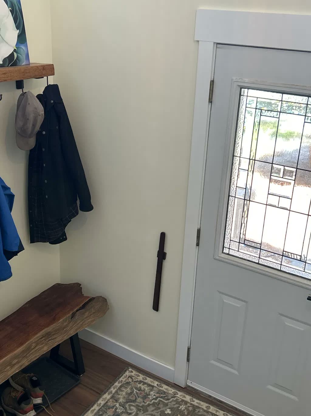 Schoenlepel van donker notenhout aan een lichte halmuur met een boomstambankje, kapstok en een voordeur met glas-in-lood