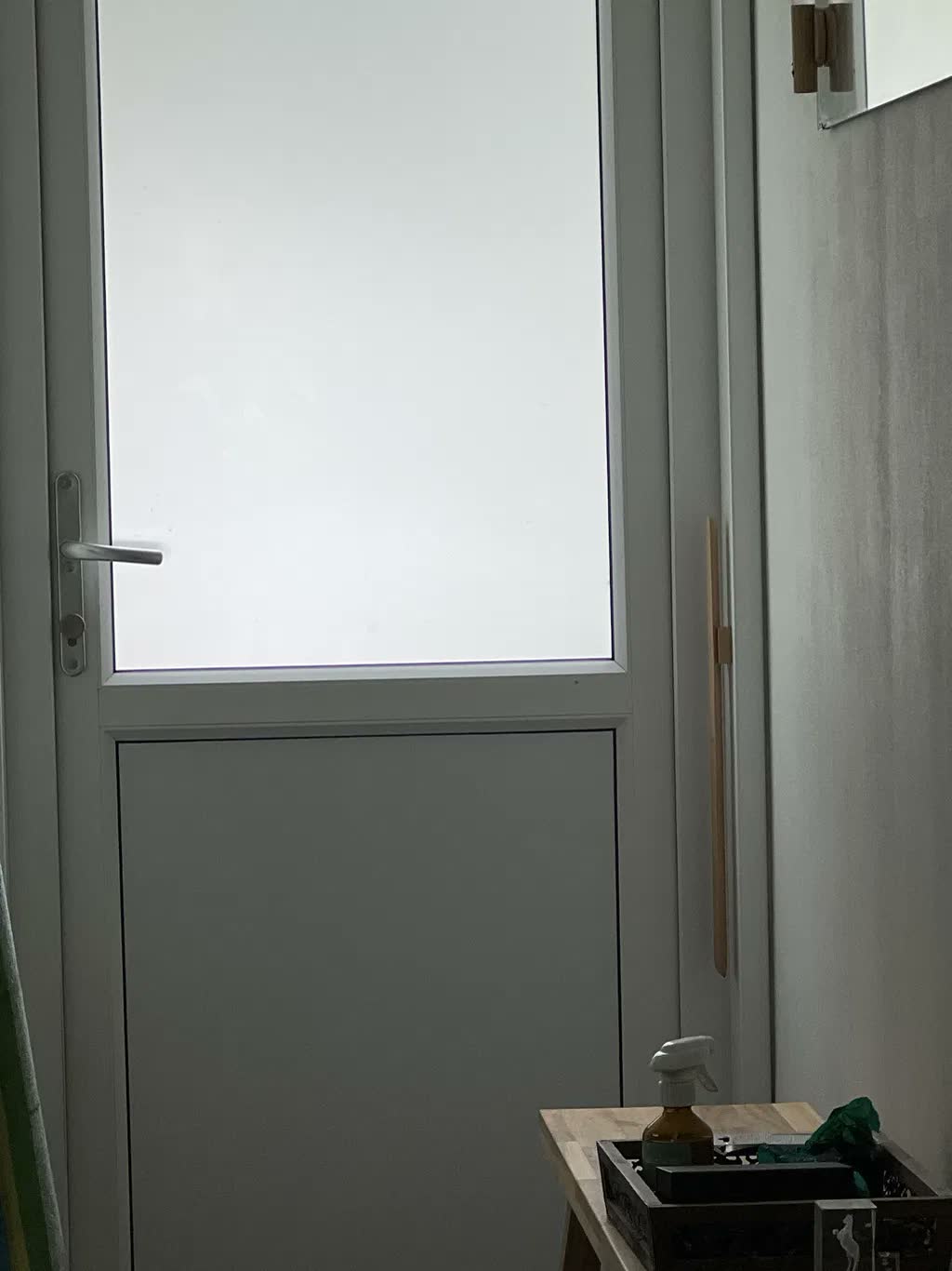 Schoenlepel van naturel beuken aan een grijze muur naast een witte tuindeur met matglas